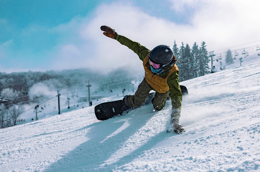 Man riding snowboard with left hand on the snow, and right hand in the air.